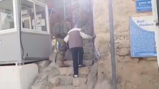 جندي إسرائيلي يساعد عجوز فلسطيني في صعود السلم