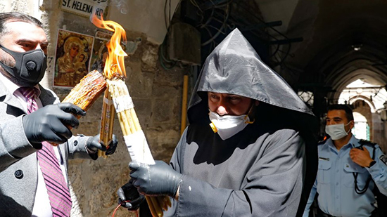 كاهن ينقل الشعلة في أحد شوارع القدس وهو يرتدي كمامة