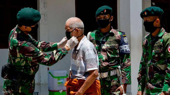 عناصر من الجيش الإندونيسي يساعدون مسنا في ارتداء كمامة